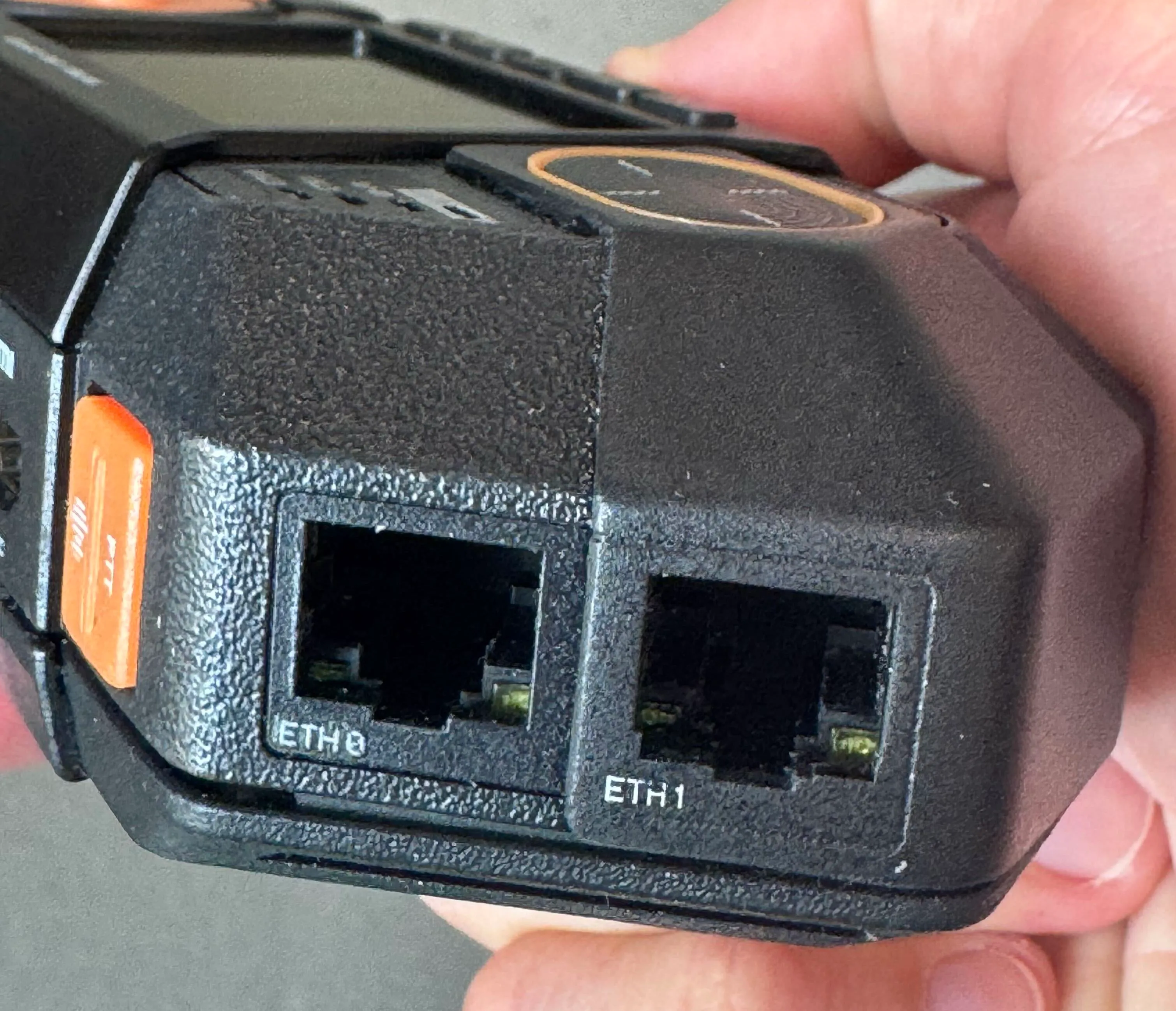 Photo of a hand holding Flipper One, showing the two Ethernet ports with visible connector LEDs